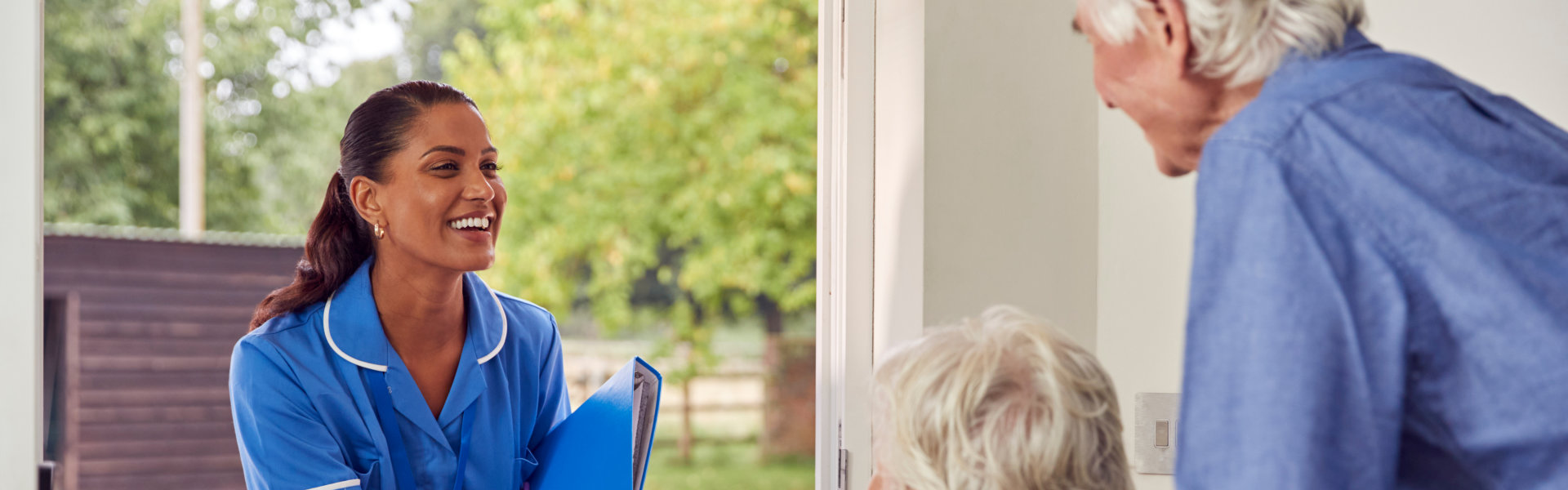 Senior Couple With Woman In Wheelchair Greeting Nurse